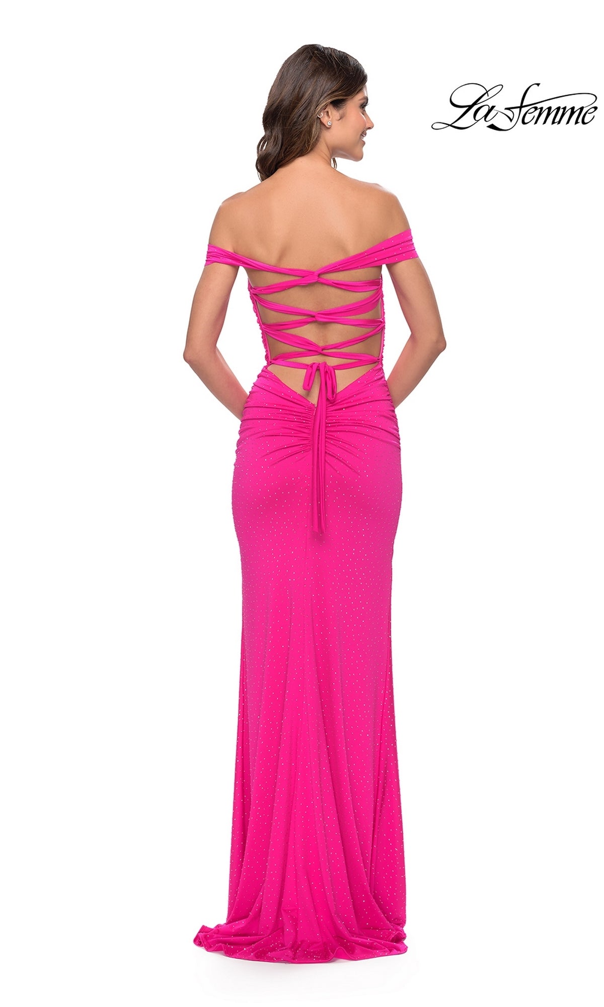 A woman is shown from behind wearing the La Femme Off-Shoulder Long Beaded Prom Dress 31276 in bright pink, featuring a lace-up back, subtle sparkling accents, and an off-the-shoulder design.